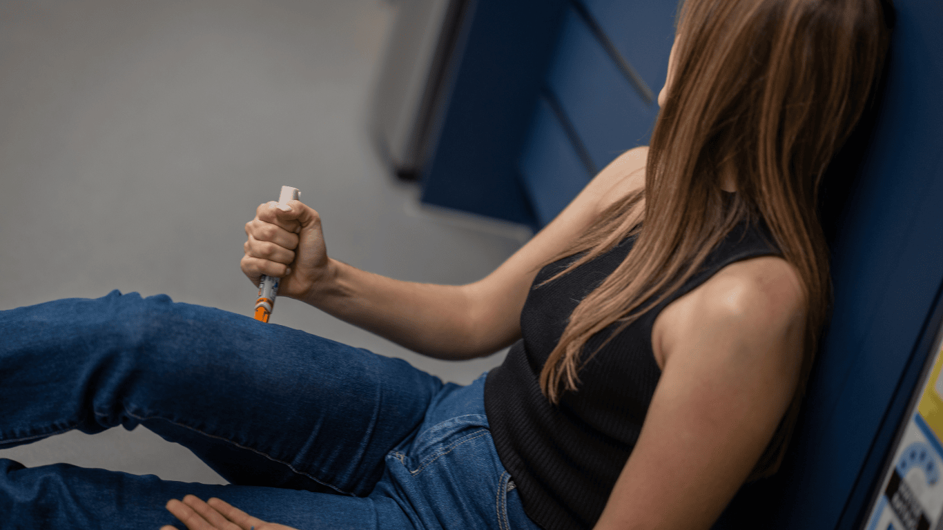 Chica sentada en el suelo inyectándose adrenalina a sí misma por una reacción alérgica grave